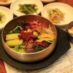 Jeonju bibimbap in a brass bowl with side dishes on the table